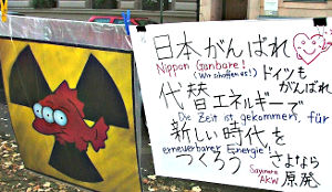 Zwei Plakate: 1. Atomwarnzeichen mutiert zum Strahlenmonster. 2. Schrifttafel mit japanischen Antiatomlosungen mit deutscher Übersetzung.