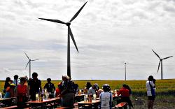 Landschaft mit Windkraftanlagen. Vorn rastet Bike for Peace and New Energies an gedeckten Tischen.